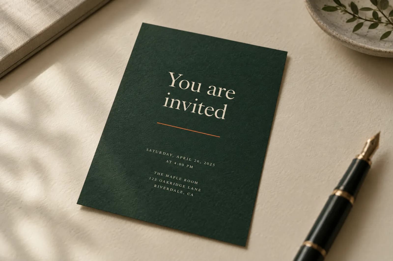 A printed pine-green invitation card on cream paper, lit from a window.
